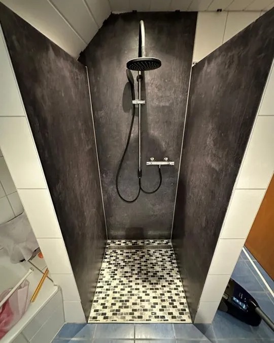 Eine moderne Dusche mit dunklen Wänden und einem schwarz weißen Mosaikboden