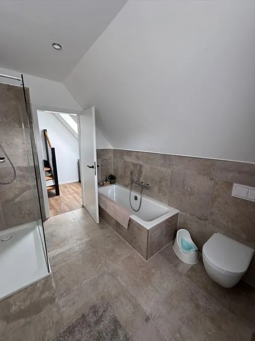 Modern Badezimmer mit beigen Fliesen, Badewanne, Dusche, WC und offenem Dachfenster