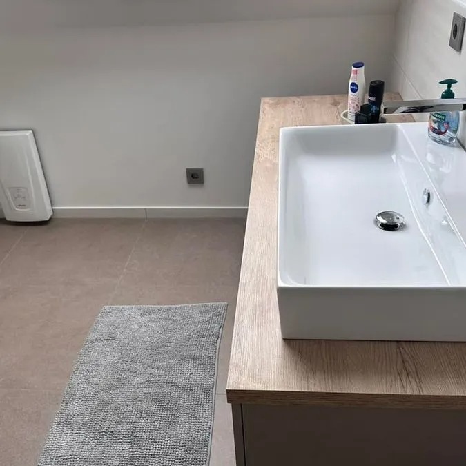 Modern Waschbecken auf Holzplatte mit Seifenspender, Zahnbürste und grauem Teppich