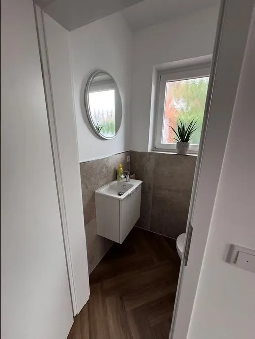 Helles kleines Gäste WC mit weißem Waschbecken, rundem Spiegel und einer Pflanze