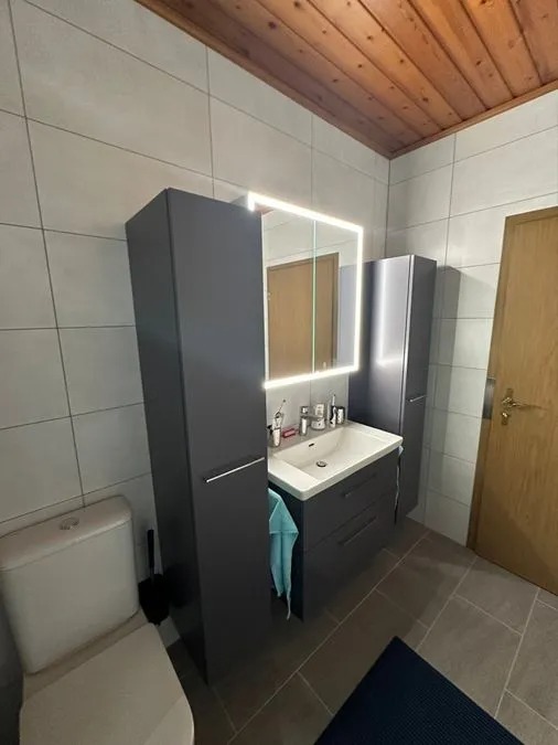 Modern graues Badezimmer mit beleuchtetem Spiegel und weißer Keramiktoilette