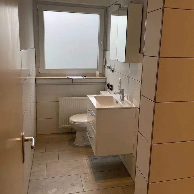 Ein modernes Badezimmer mit weißer Keramik, kleinem Waschbecken und großem Fenster