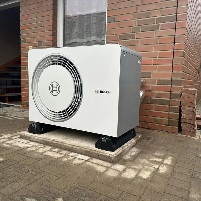 Eine moderne weiße Bosch Wärmepumpe steht vor einem Backsteingebäude auf Pflastersteinen