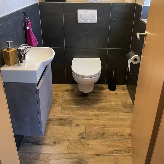 Modern Badezimmer mit hängendem WC, Holzoptik Boden und pinkem Handtuch am Waschbecken
