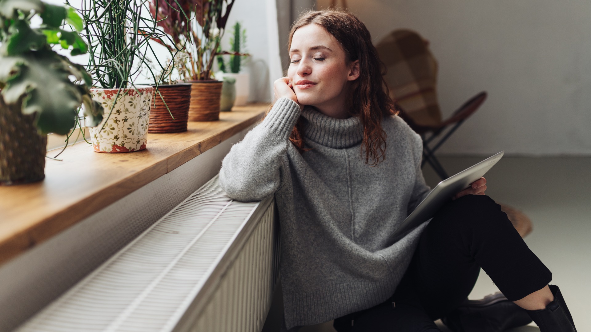 Junge Frau entspannt an der Heizung mit Tablet in der Hand