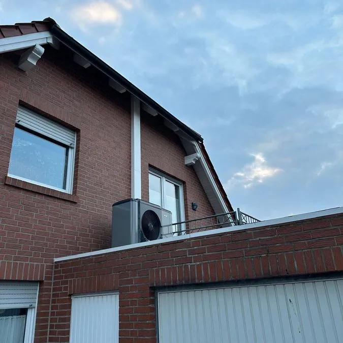 Backsteinfassade eines Hauses mit weißem Fenster und einer grauen Klimaanlage auf dem Dach