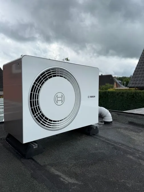 Eine weiße Bosch Klimaanlage steht auf einem dunklen Dach unter bewölktem Himmel