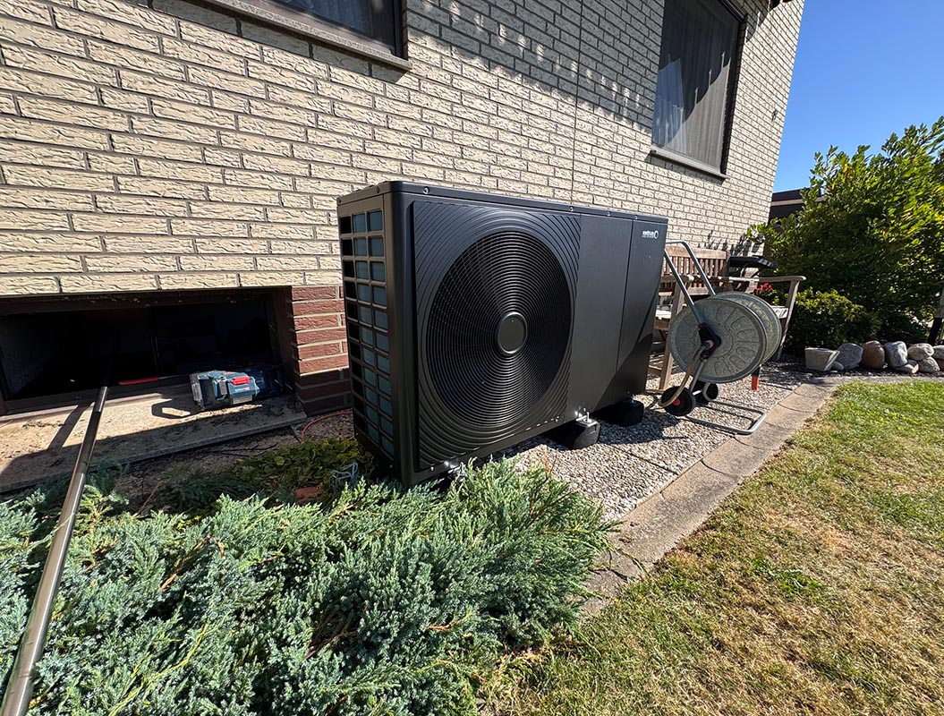 Eine große schwarze Wärmepumpe steht neben einem Haus mit hellem Mauerwerk im Garten