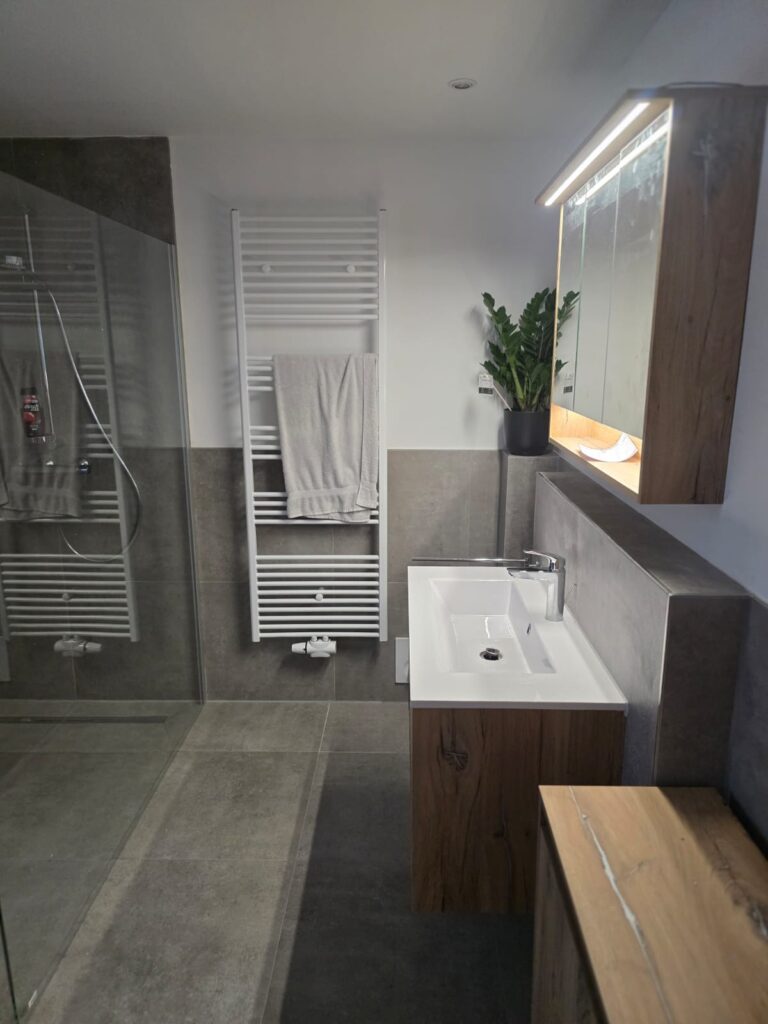 Modern Badezimmer mit weißem Waschbecken, Holzunterschrank, beleuchtetem Spiegel und einer Pflanze