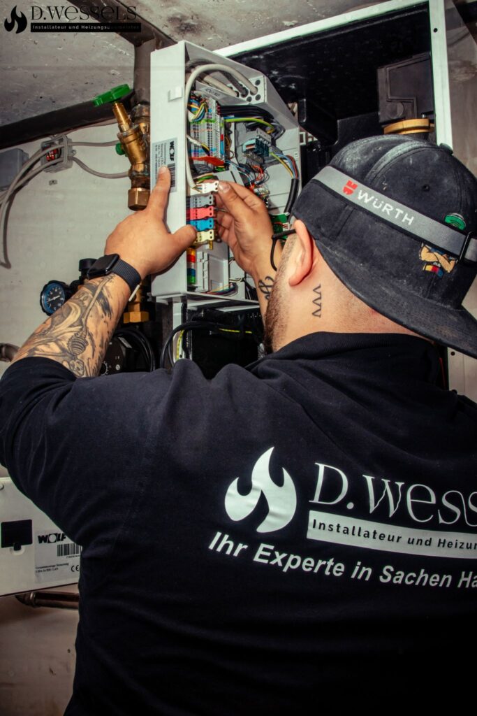 Ein Mann mit Bart und Tattoos wartet konzentriert ein technisches Heizsystem in einem weißen Kasten