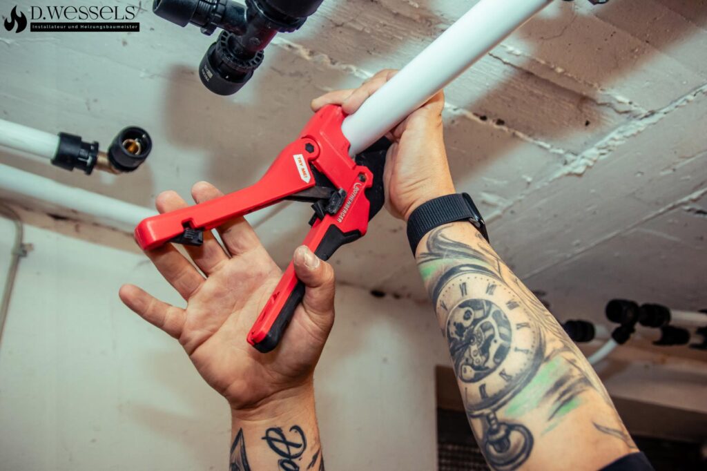 Eine tätowierte Person klemmt konzentriert ein weißes Rohr mit einer roten Zange ab