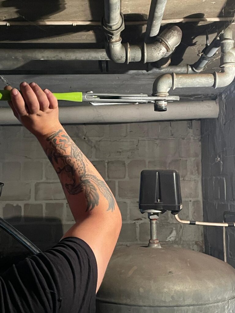 Ein Mensch mit Drachen Tattoo am Arm arbeitet konzentriert an einer Rohrleitung